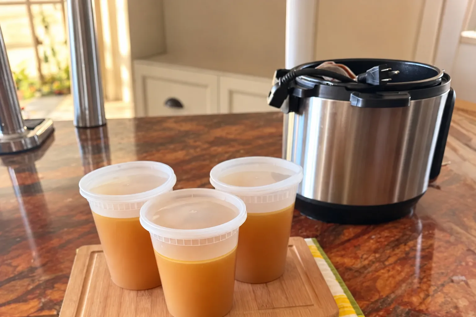 Three one-quart containers of homemade chicken stock beside an electric pressure cooker.
