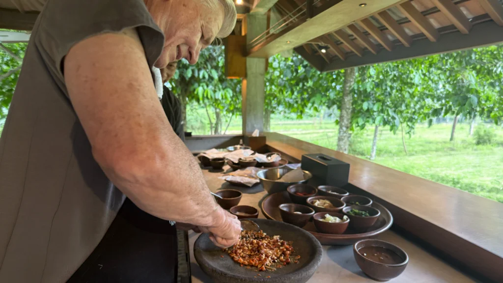 John grinding spices with a stone mortar in an open-air kitchen.